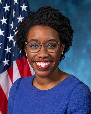 Headshot of U.S. House of Representative Lauren Underwood wearing a cobalt blue top. There's an American flag behind her right shoulder.