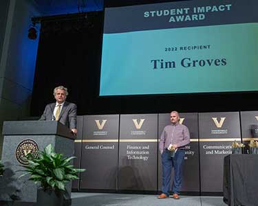Chancellor stands at podium. VUSN staff Tim Groves stands under a slide that reads "Student Impact Award--Tim Groves"