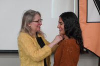Woman in yellow sweater pins a nursing pin on female student