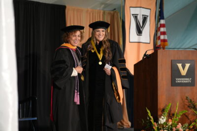 Two women wearing graduation robes smiling.