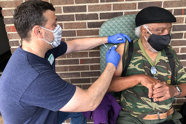 Male volunteer gives a vaccine shot to an older gentleman
