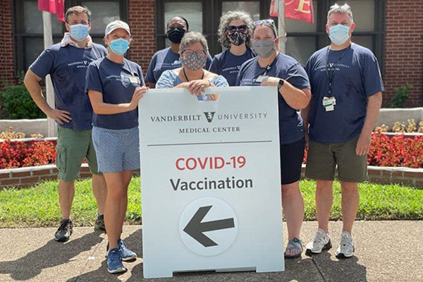 Vaccine volunteers with a sign announcing Vanderbilt Health & Vanderbilt School of Nursing COVID-19 Vaccination followed by a big arrow