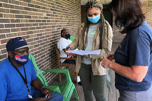 Older gentleman wearing a mask waits to fill out paperwork to get a COVID vaccine while a student and faculty member review it.