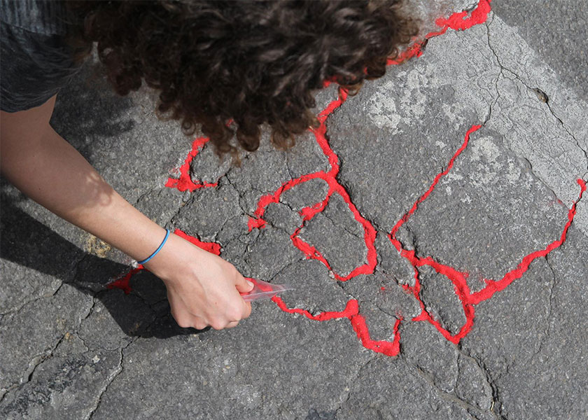 Person pouring red sand into sidewalk cracks