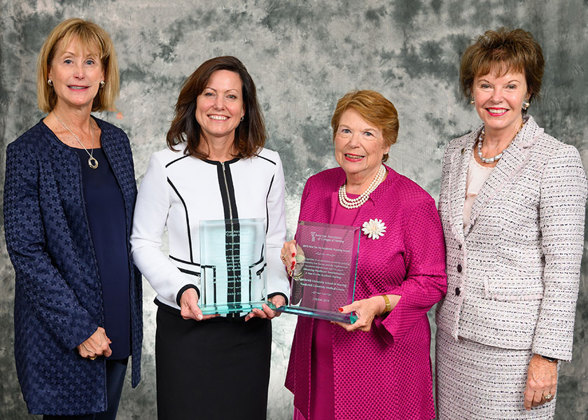 Four women in business dress with two holding big engraved glass awards. The women are Left, AACN President and CEO Deb Trautman, April Kapu, Linda Norman and AACN Board Chair Ann Cary