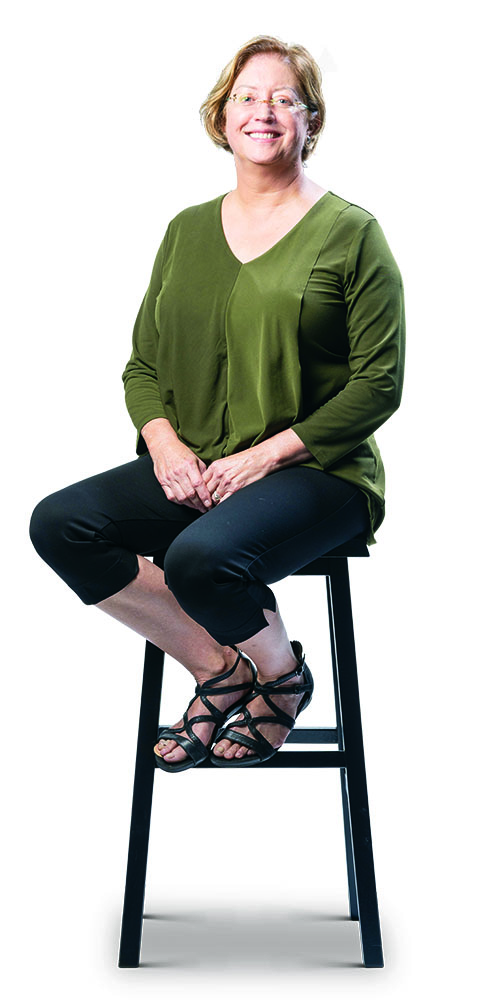 Shelagh Mulvaney in green top and dark capris, sitting on a stool.