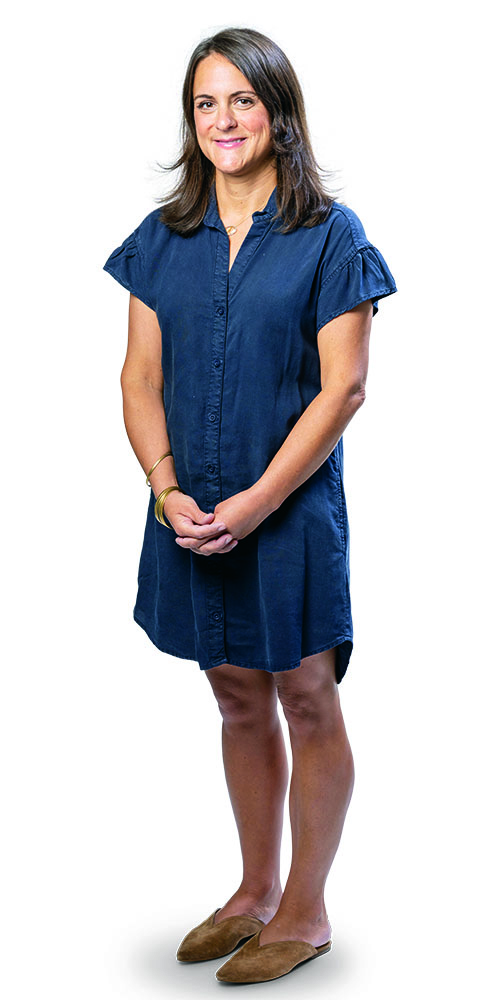 Sarah Wray in blue shirtdress standing.