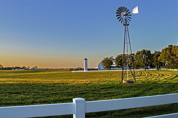 Rural image of a windmill in a field with farm behind it