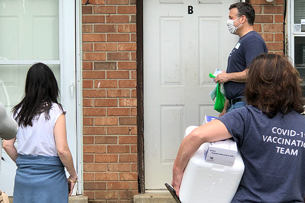 Three people outside a house with mobile vaccine to administer