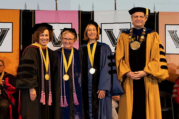 Four people in academic robes pose for a photo.