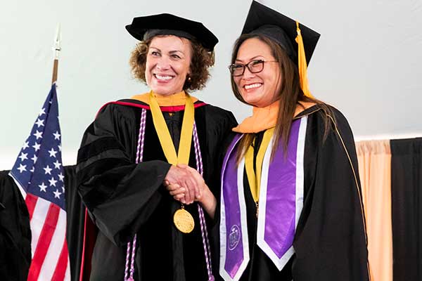 Dean Pam Jeffries in academic regalia shakes hand of Founder's Medalist Tip Tilton, who is also in regalia