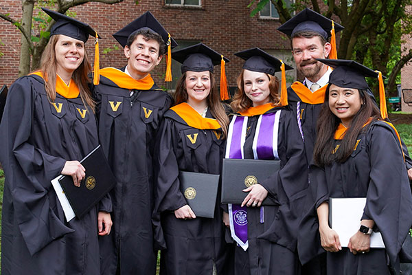 6 graduates in caps and gowns hold their diplomas