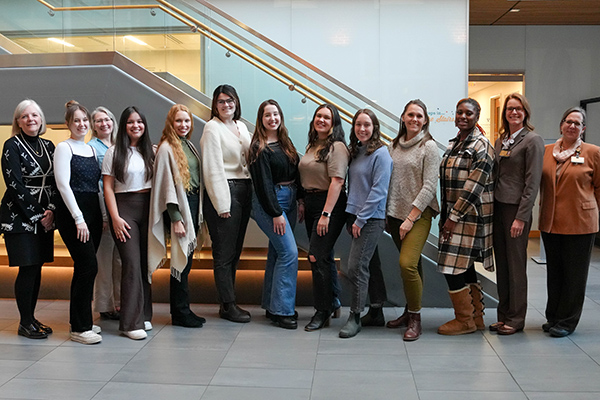 Group of 13 women stand in front of a modern looking staircase