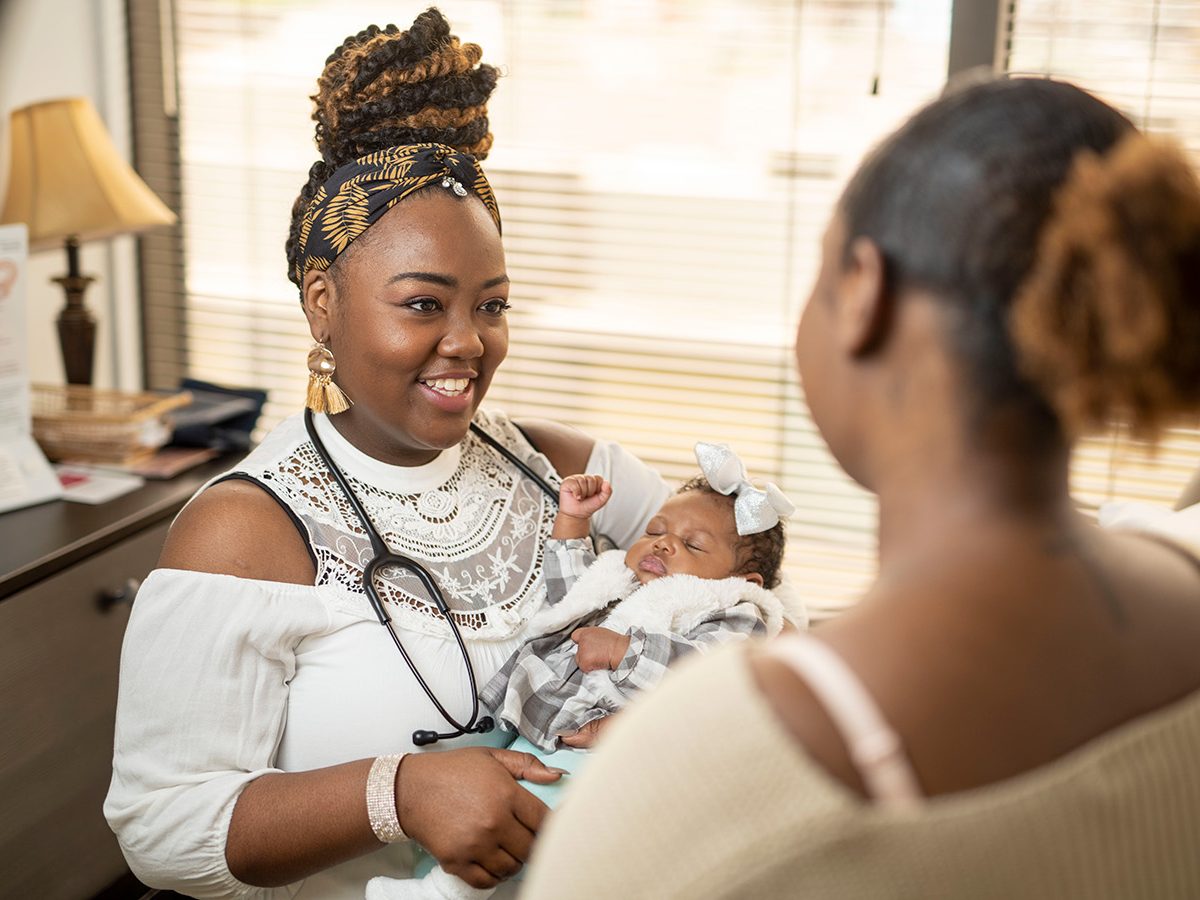 Alumnus and CNM holds infant while talking to the child's mother