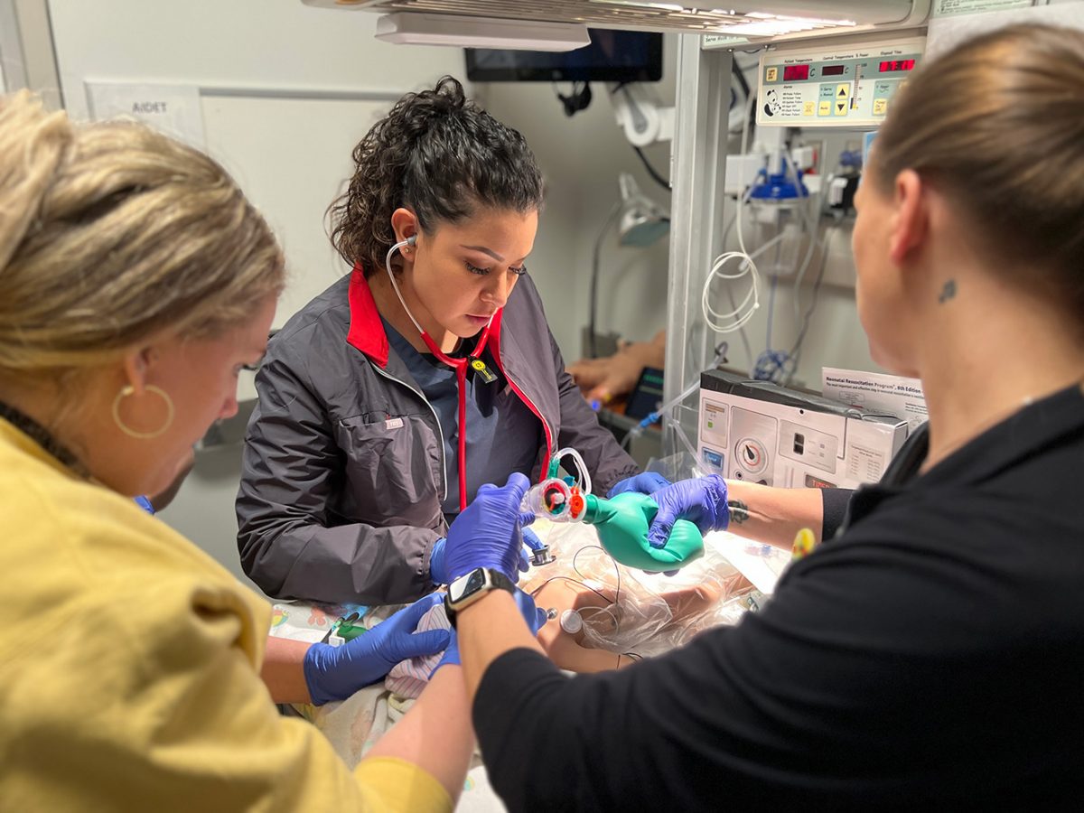 Three nurse practitioner students resuscitate an infant in a simulation with a mannequin.