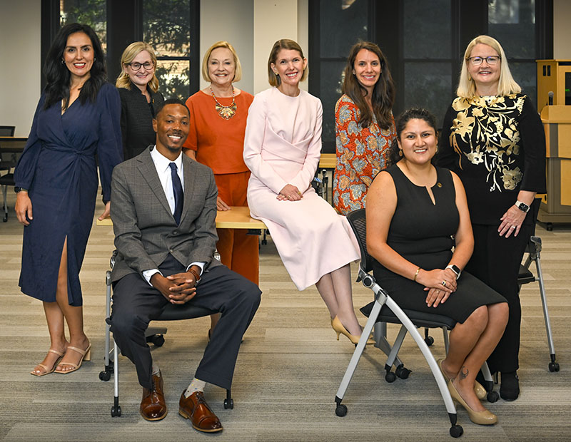 Group of 7 women and one man in business/formal dress pose for a group photo