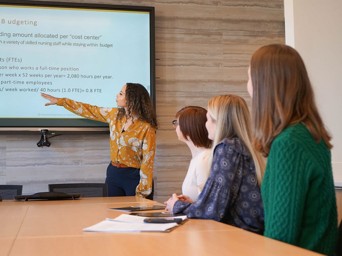 Health care and Nursing Leadership student gestures to material on a screen while three other students listen.