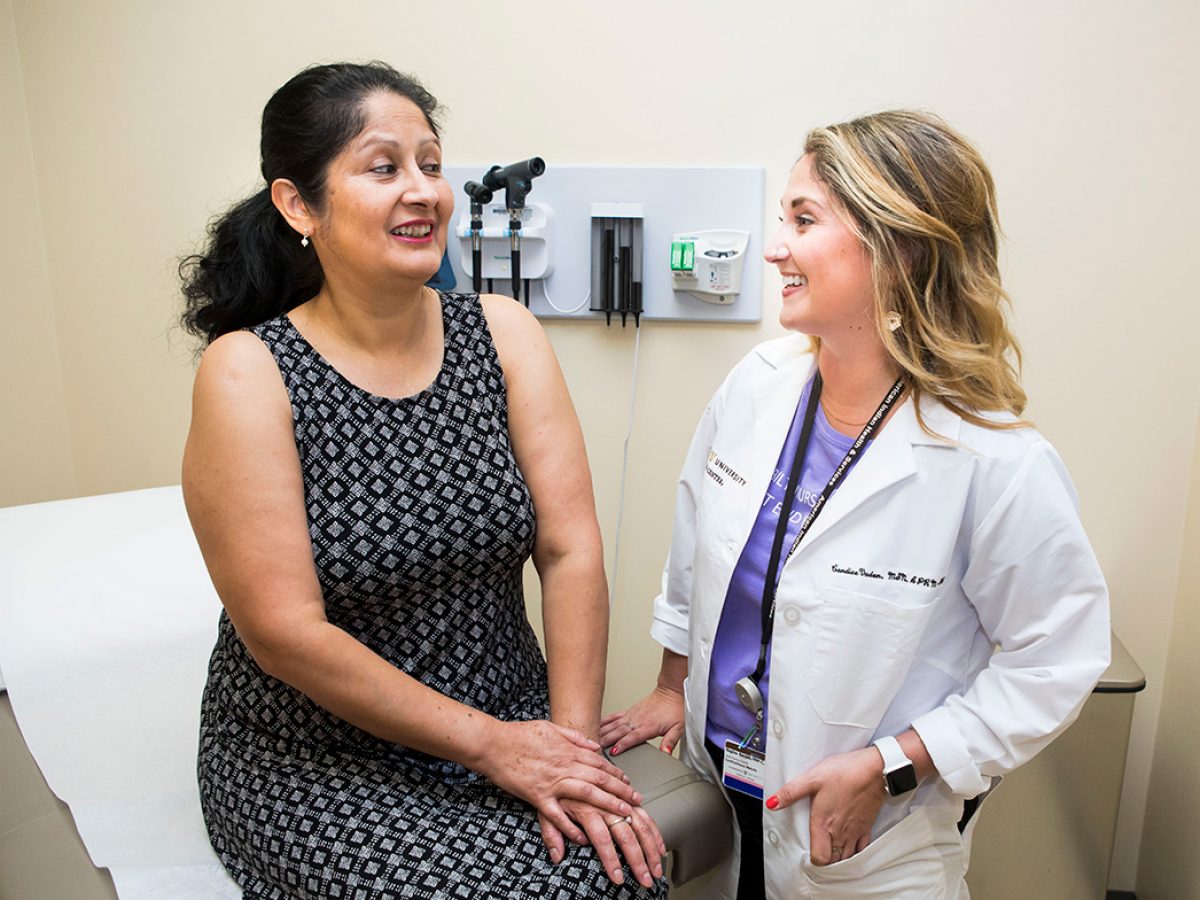 Nurse practitioner in a white coat talks to a female patient in an exam room.