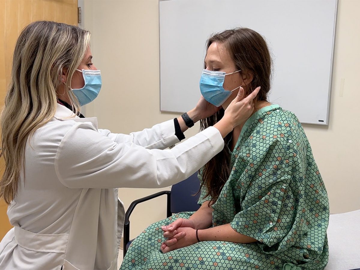 Pediatric nurse practitioner student examines a teen in an exam room. Both wear masks.